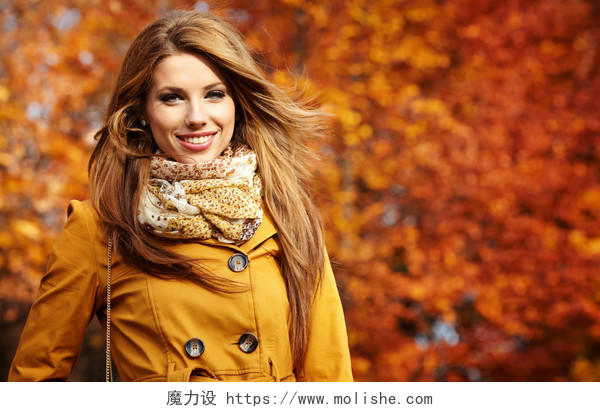 年轻女子手握秋叶落在黄枫园的背景下